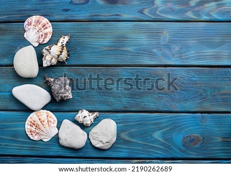 White pebbles, flat shells and sea shells on bright blue boards. Blue wooden background with orange streaks. Space for text