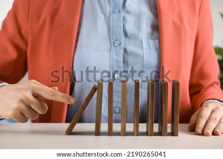 Woman causing chain reaction by pushing domino tile at table, closeup Royalty-Free Stock Photo #2190265041
