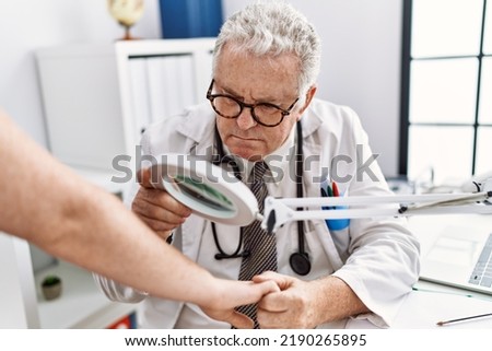 Middle age grey-haired man wearing dermatologist uniform examining skin arm using loupe at dermatology clinic Royalty-Free Stock Photo #2190265895