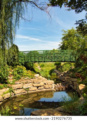 Green bridge in the middle of a flower garden in Overland Park Kansas on a hot sunny Summer day. Royalty-Free Stock Photo #2190276735