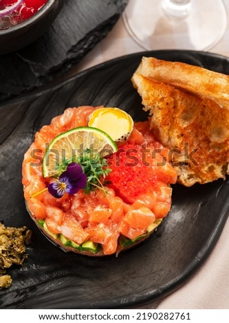 Overhead View on Salmon Tartar with Red Caviar and Toast on Black Plate for Recipe Book, Blog, Food or Travel Magazine, for Lightbox for Catering Premises