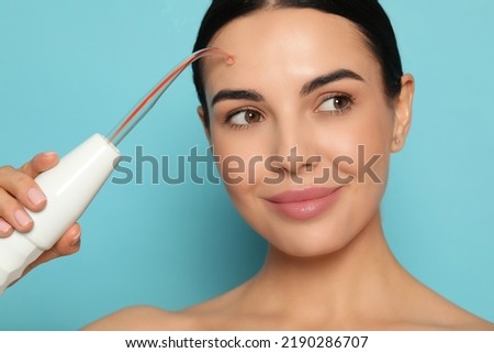 Woman using high frequency darsonval device on light blue background Royalty-Free Stock Photo #2190286707