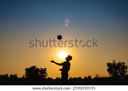 Silhouette action sport outdoors of kids having fun playing soccer football for exercise in community rural area under the twilight sunset sky. Picture with copy space.