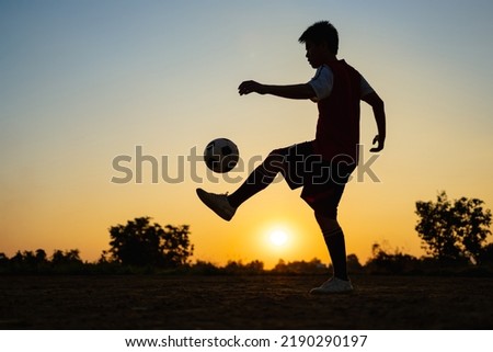 Silhouette action sport outdoors of kids having fun playing soccer football for exercise in community rural area under the twilight sunset sky. Picture with copy space.