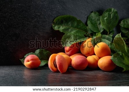 Apricots with leaves on a black stone table.