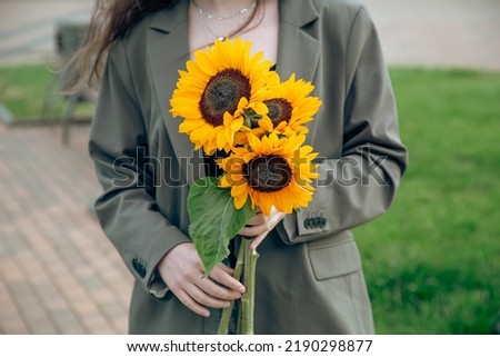 Close-up, a bouquet of sunflowers in female hands on a blurred background.