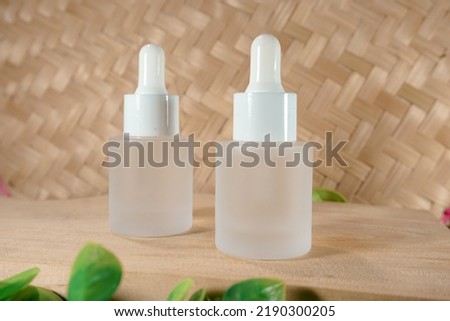 Glass dropper bottle with a white rubber dropper tip and leaves on a beautiful woven bamboo background. Serum dropper bottle. Aromatherapy eyedropper jar. Cosmetic Serum. Trendy nature concept.