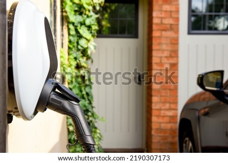 Electric car plugged in to charge outside home with power cable Royalty-Free Stock Photo #2190307173