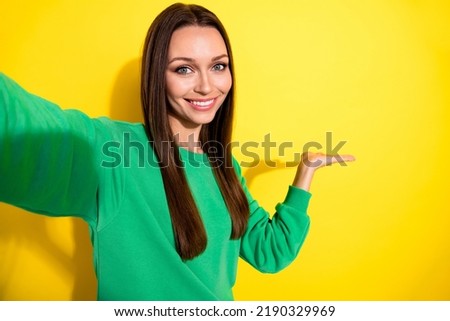 Photo portrait of pretty young woman take selfie palm holding copyspace dressed trendy green sweatshirt isolated on yellow color background