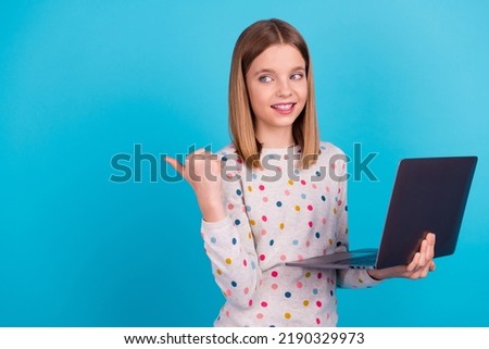 Photo of sweet shiny small girl wear dotted shirt modern device looking thumb back empty space isolated blue color background