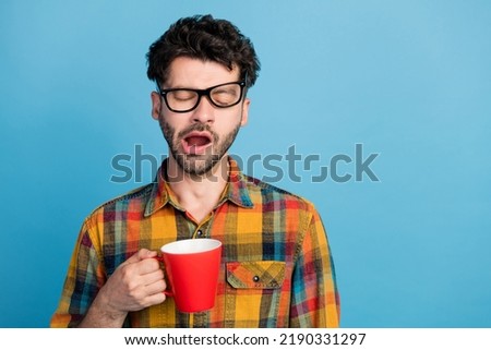 Photo of tired slumber man in eyeglasses wear checkered shirt yawn drink coffee trying to wake up isolated on blue color background Royalty-Free Stock Photo #2190331297
