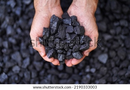Coal grains in man coal miner's hands over a pile, closeup. Coal house heating and home heating energy. Mining industry and environment protection.  Coal air polution. Closeup Royalty-Free Stock Photo #2190333003