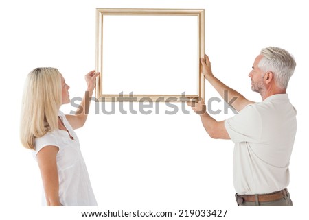 Rear view of mature couple hanging up picture frame over white background
