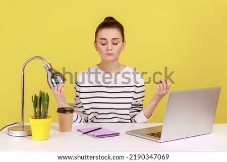Peaceful mind, break at work. Calm woman sitting at workplace with laptop and raising hands in mudra gesture, meditating resting at home office. Indoor studio studio shot isolated on yellow background Royalty-Free Stock Photo #2190347069
