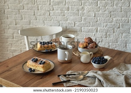 Still life in scandinavian style on a wooden kitchen table. Coffee, homemade cakes and fresh blueberries for breakfast. Concept for good morning wishes. Kinfolk style life. Horizontal photo.

