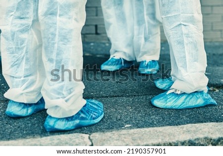 Legs and feet of healthcare workers wearing protective gear or hazmat suits outdoors while cleaning. Closeup of a team of medical professionals meeting during the covid or coronavirus pandemic Royalty-Free Stock Photo #2190357901