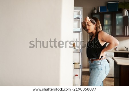 Plus size, chubby and hungry woman looking in a fridge, thinking of food or searching for meal while on a diet. Stressed, anxious and frustrated lady struggling with weight loss management Royalty-Free Stock Photo #2190358097
