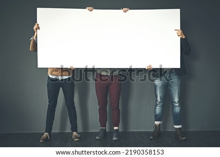 Group of businesspeople holding up a copyspace sign voicing their opinion at work with a grey background. People with blank poster advertising, marketing and express or convey important messages Royalty-Free Stock Photo #2190358153