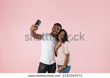 Joyful people using mobile phone to take selfies together in studio . Man and woman showing tongue taking picture with smartphone and having fun in front of camera. Carefree couple feeling happy.