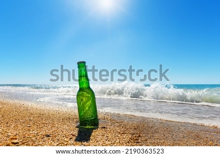 A bottle of beer on the beach against the backdrop of sea waves and bright sun.