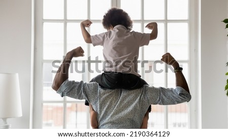 Rear view African American father and little son sitting on dad shoulders showing biceps, strength, healthy lifestyle and fit concept, playing active game, two superheroes, support and care Royalty-Free Stock Photo #2190364129