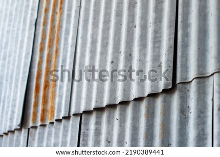 Multiple sections of galvanized weathered corrugated metal panels on the exterior wall of an old barn and building. There are sections of rust along the vertical rows of grey weathered siding plates. Royalty-Free Stock Photo #2190389441