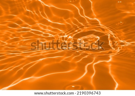 Defocus blurred transparent orange colored clear calm water surface texture with splashes and bubble. Trendy abstract nature background. Water wave in sunlight with copy space. Orange water drop color