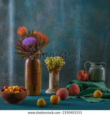 Still life on a blue-green background with artichoke flowers, peaches, grapes, and plums.