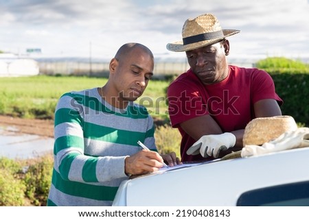 Two males farm workers signing documents near car outdoors