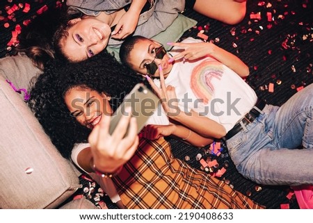 Cute selfies only. High angle view of three happy friends taking a selfie while lying on the floor at a house party. Group of cheerful female friends having fun together on the weekend.