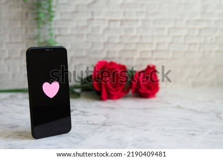 A smartphone with a heart mark, a rose and a front facing photo of a marble background on the left Royalty-Free Stock Photo #2190409481