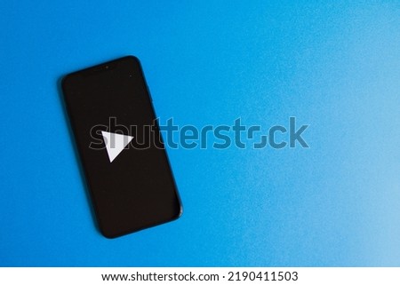 A smartphone with a play mark and a bird's-eye view of the left side of the blue background