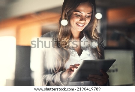 Working late, overtime and dedication with a happy, positive and motivated business woman working on a tablet in her office. Young female executive smiling while feeling dedicated and determined Royalty-Free Stock Photo #2190419789