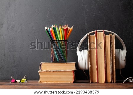 Old books and headphones on wooden table and blackboard for copy space. Audiobooks and education template