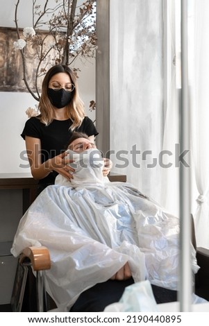 Vertical photo of a man sitting on a comfortable chair receiving a facial treatment in a salon
