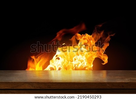 Side view of an empty wooden tabletop with orange fire or flames and sparkles on a dark background.
