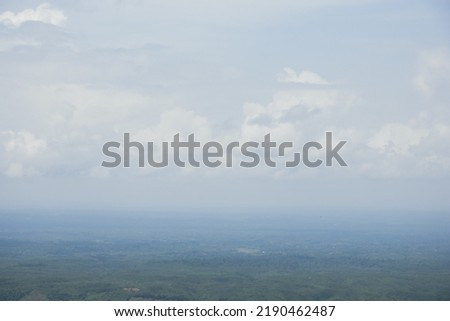 Aerial landscape view with a drone of meadow and cloudy sky horizon. Beautiful natural view of green fields and sky. Foggy weather drone shot of a hilly jungle area and sky horizon. Royalty-Free Stock Photo #2190462487