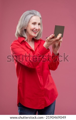 Mature woman in red doing makeup and looking contented