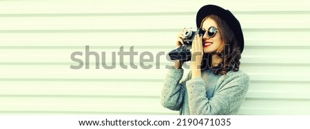 Portrait of young woman photographer with film camera wearing knitted sweater cardigan, black round hat on white background