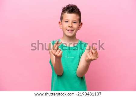 Little caucasian boy isolated on pink background making money gesture