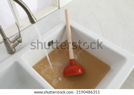 Clogged kitchen sink with plunger and dirty water Royalty-Free Stock Photo #2190486351