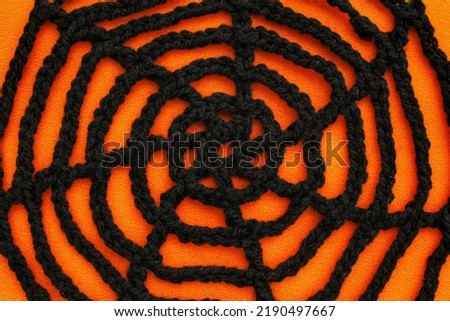 Black crochet spider web on orange background with copy space for text. Halloween autumn decoration scary creepy horror concept. Idea for banner, postcard, poster. Spooky Cobweb. Flat lay, mock up