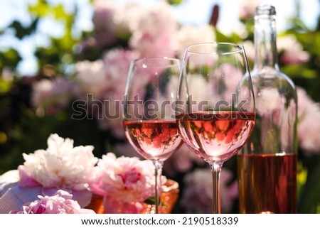 Bottle and glasses of rose wine near beautiful peonies in garden, closeup. Space for text