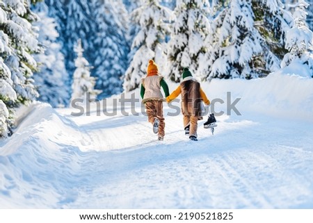 Winter family walk along a wonderful snowy forest road. Children run snow, back view. Sunny winter day.