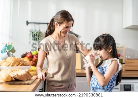 Asian little cute kid holding a cup of milk and drinking with mother. Attractive mom teach and support young girl daughter take care of her body, sipping a milk after wake up for health care in house. Royalty-Free Stock Photo #2190530881