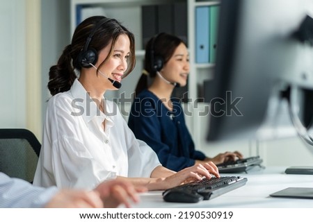 Two Asian beautiful businesswoman call center work in office corporate. Attractive young employee worker people sit on table, wear headset and use laptop computer talk to support customer at workplace Royalty-Free Stock Photo #2190530919