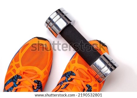 A metal heavy dumbbell fell on a leg in orange torn sneakers on a white background. Life to the sport.