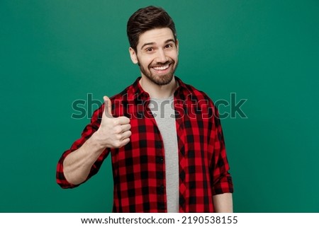 Young happy smiling satisfied positive fun cool man he 20s wearing red shirt grey t-shirt showing thumb up like gesture isolated on plain dark green background studio portrait People lifestyle concept