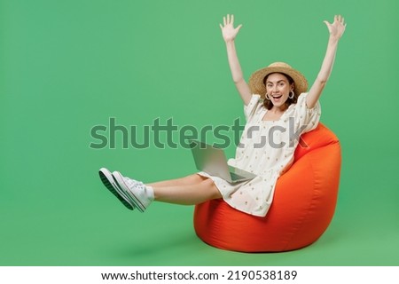 Full body young happy overjoyed fun woman she 20s wears white dress hat sit in bag chair hold use work on laptop pc computer raise up hands legs isolated on plain pastel light green background studio.