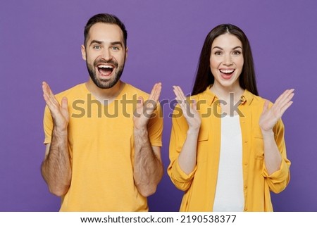 Young surprised excited shocked amazed fun couple two friends family cool man woman 20s together in yellow casual clothes look camera spread hands isolated on plain violet background studio portrait